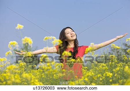 Young woman standing in the flower field with arms outstretched View Large Photo Image Stock Image - Young woman standing in the flower field with arms outstretched. Fotosearch