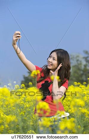 Stock Image - Young woman taking pictures in the flower field. Fotosearch