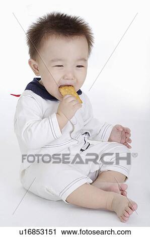 Stock Image - Baby boy sitting and eating biscuit, Child. Fotosearch