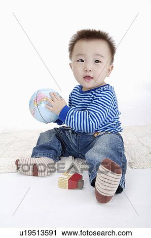 Stock Image - Baby boy sitting and holding a globe, Child. Fotosearch