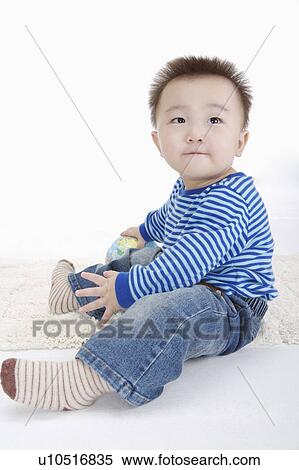 Stock Photography - Baby boy sitting and playing with a toy, Child. Fotosearch