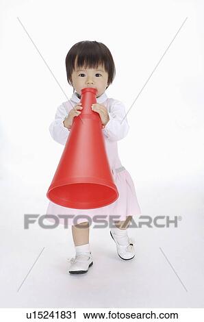 Stock Image - Baby girl standing and holding a toy speaker, Child. Fotosearch