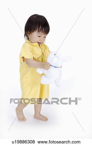 Stock Photo - Baby girl standing and holding a toy, Child. Fotosearch