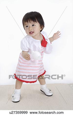 Stock Photo - Baby girl standing and holding a toy, Child. Fotosearch