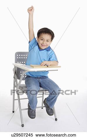 Stock Photography - Boy sitting on chair with one hand raised and looking at the camera, Child. Fotosearch