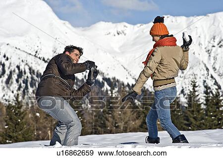 Young man photographing young woman holding snowball in winter scene View Large Photo Image Stock Photo - Young man photographing young woman holding snowball in winter scene. Fotosearch