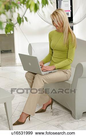 Young business woman working on laptop in a modern hotel lounge, public phone in background View Large Photo Image Stock Photo - Young business woman working on laptop in a modern hotel lounge, public phone in background. Fotosearch