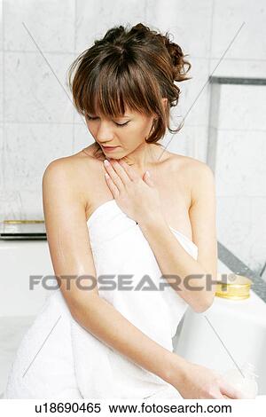 Stock Photography - Young woman in bathroom, applying body lotion. Fotosearch
