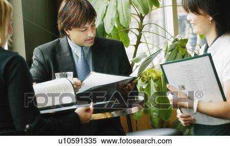 Stock Photography - Businessman looking at menu in restaurant. Fotosearch