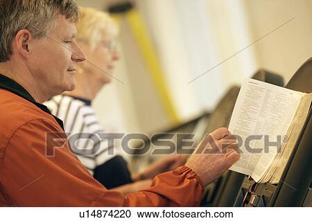 Stock Image - Man and woman reading on stationary bike. Fotosearch