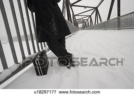 Stock Photo - Man with briefcase waiting on snow covered bridge. Fotosearch