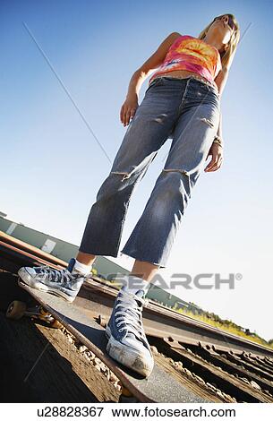 Stock Photo - Woman on skate board on train tracks. Fotosearch