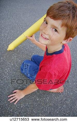 Stock Image - A close-up (close up closeup) of a child sitting on asphalt with an oversized yellow crayon.. Fotosearch