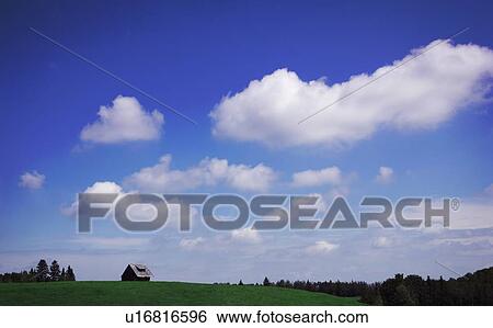 Stock Photograph - A cloudy sky and a field with a building. Fotosearch