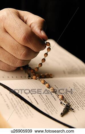 Stock Photo - A hand holds a rosary and bible. Fotosearch