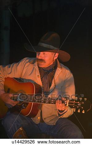 Stock Photograph - Cowboy playing guitar at the campfire. Fotosearch