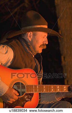 Picture - Cowboy Playing guitar by campfire. Fotosearch