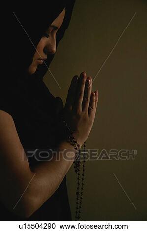 Stock Image - Teen praying with prayer beads. Fotosearch