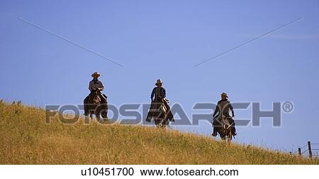 Stock Image - Three cowboys coming over the hill. Fotosearch
