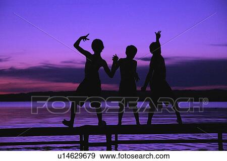 Stock Photo - Three silhouettes of boys on a dock against a sunset. Fotosearch