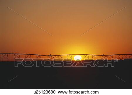 Stock Image - Irrigation system silhouette at sunset. Fotosearch