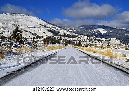 Stock Image - Snow-covered highway with mountain backdrop. Fotosearch