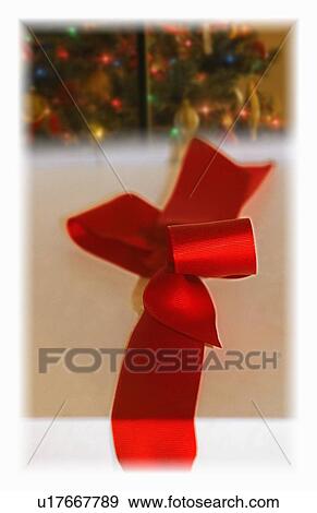 Stock Photo - Tied red ribbon with Christmas tree in background. Fotosearch