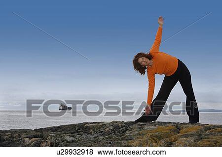 Stock Photo - Woman stretching on a rocky beach. Fotosearch