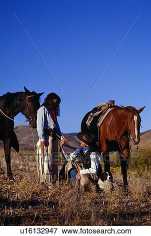 Stock Photo - Cowboy and cowgirl holding hands beside their resting horses, Ponderosa Ranch.. Fotosearch