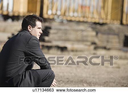 Stock Image - Man in a pinstriped suit bending down. Fotosearch