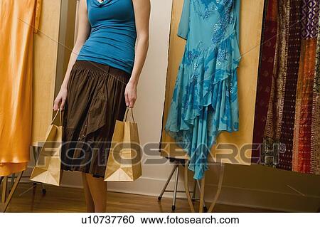 Stock Image - Woman standing in dressing room with shopping bags. Fotosearch