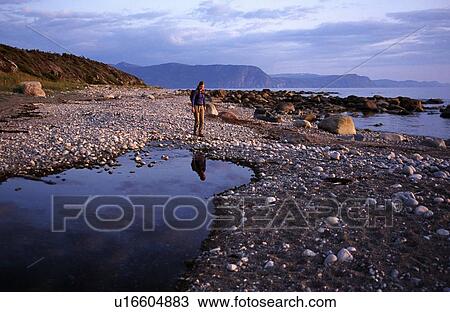 Stock Image - Hiker walking on beach with tide pools. Fotosearch