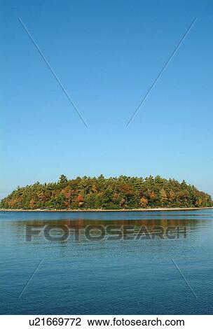 Stock Image - A forested island in a lake against a blue sky and blue water. Fotosearch