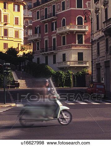 Stock Photo - Blurred image of teenager on scooter with backdrop of apartment buildings. Fotosearch