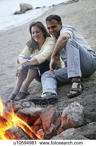 Stock Image - Couple keep warm by campfire. Fotosearch