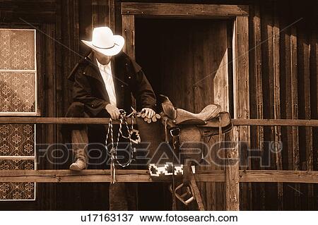 Stock Photo - Cowboy with saddle and lariat over handrail in front of building. Fotosearch