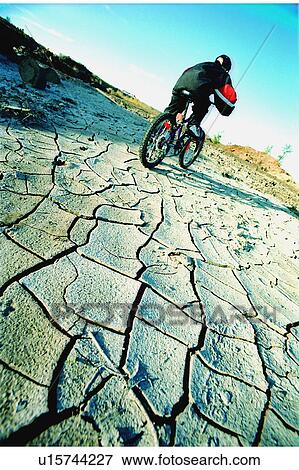 Stock Photo - Cyclist riding on dried and cracked mud. Fotosearch