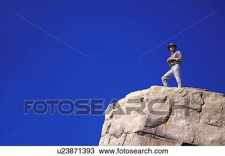 Stock Image - Hiker with binoculars on cliff edge. Fotosearch