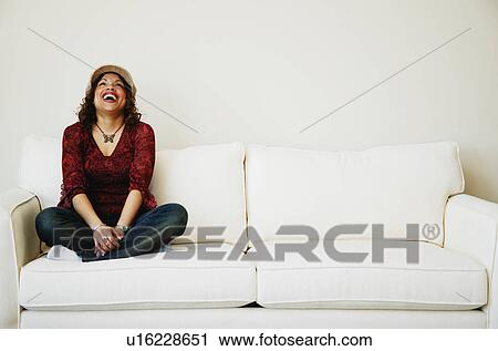 Stock Image - Laughing woman sitting on sofa. Fotosearch