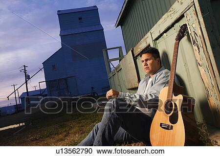 Stock Image - Man sits beside guitar. Fotosearch