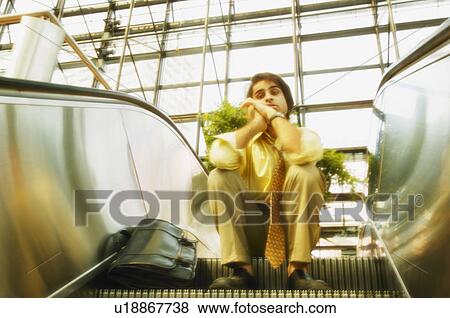 Stock Photo - Man sits on an escalator. Fotosearch