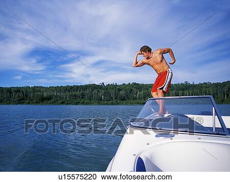 Stock Image - Man standing on rear of boat while flexing muscles. Fotosearch