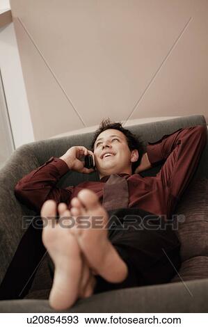 Stock Image - Man talking on cell phone while relaxing on couch. Fotosearch