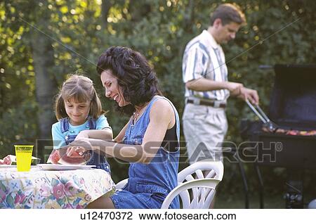 Stock Image - Mother and daughter eating watermelon at picnic. Fotosearch