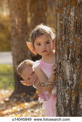 Two fairy girls peering from behind a tree in the Autumn forest View Large Photo Image Stock Photo - Two fairy girls peering from behind a tree in the Autumn forest. Fotosearch