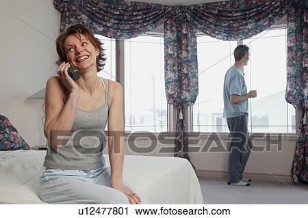 Stock Image - Wife chats on phone while husband waits. Fotosearch