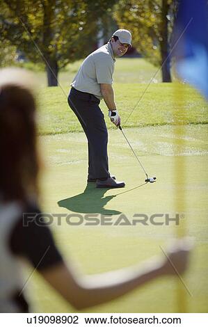 Stock Image - Woman holds flag on putting green. Fotosearch