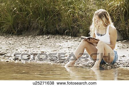 Stock Photo - Woman reads book with feet in water. Fotosearch