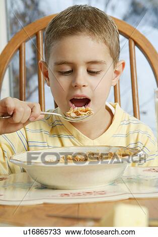 Stock Image - Young boy eating cereal at breakfast table. Fotosearch
