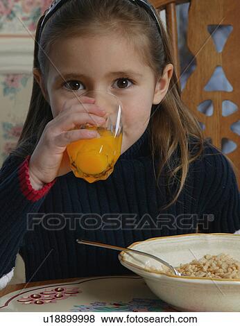 Stock Photo - Young girl drinking orange juice at breakfast table. Fotosearch